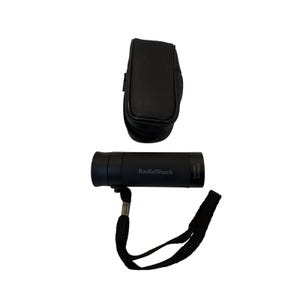 May include: A black RadioShack monocular with a wrist strap and a matching black carrying case. The monocular has the text "RadioShack" printed on the side. The carrying case is rectangular and has a flap closure.