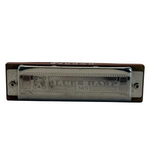 May include: A silver and brown Hohner Blues Harp harmonica. The harmonica has a rectangular shape with the words "Blues Harp MS" printed on the front. The harmonica is a musical instrument.