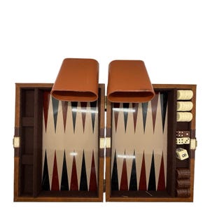 May include: Open backgammon set with a wooden case, featuring a playing surface with alternating black, red, and beige triangles. Includes brown leather dice cups, ivory-colored game pieces, and dice. The set is open and ready for play.
