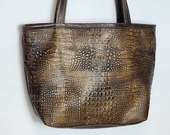 May include: A brown leather tote bag with a crocodile embossed pattern. The bag has two brown leather straps.