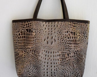 May include: A tote bag with a faux crocodile skin pattern in shades of gray and brown. The bag has a rectangular shape with a dark brown trim and matching handles. The bag is made of a textured material.