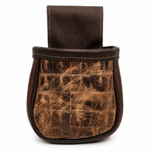 May include: A brown leather sporran featuring a textured, distressed tan and dark brown front panel with a grid-like pattern. The pouch has a smooth dark brown leather border, a matching top flap, and visible stitching along the edges.