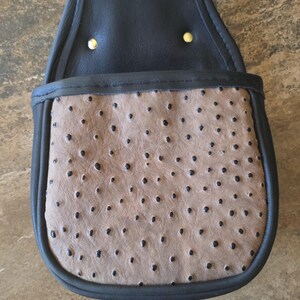 May include: A black and tan leather pouch with a flap and two gold rivets. The tan section has a textured pattern of small, dark spots. The pouch is trimmed in black and has the text "DSB-2061" at the bottom.
