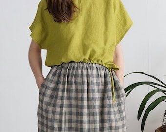 Op de afbeelding: Een limoengroene top met korte mouwen, een ronde halslijn en een geplooide taille met een strik aan de zijkant, gecombineerd met een lange rok met hoge taille in een grijs en beige ruitpatroon met elastische tailleband en zijzakken.