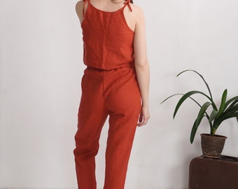 Puede incluir: Un conjunto de dos piezas compuesto por una parte superior sin mangas con tirantes finos y pantalones largos a juego en un color naranja quemado. La parte superior presenta un escote recto y los pantalones tienen un corte holgado con dobladillos.