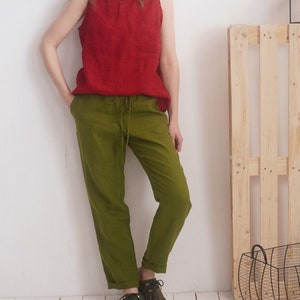 May include: A sleeveless red top and olive green pants. The pants have a drawstring waist and cuffed hems. The outfit is made of a lightweight fabric. A wooden pallet and a wire basket are in the background.