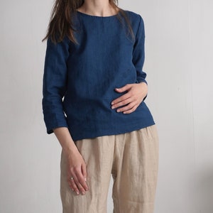 May include: A dark blue long-sleeved top with a round neckline and three-quarter length sleeves, paired with loose-fitting beige trousers. The top features a simple, straight-cut design, while the trousers have a relaxed, comfortable fit.