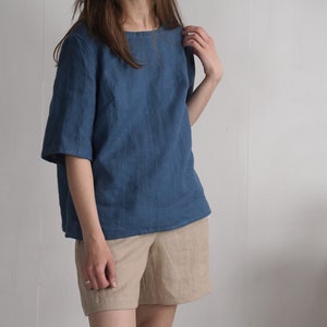 Könnte beinhalten: Ein blaues Leinenoberteil mit kurzen Ärmeln und einer lockeren Passform. Das Oberteil wird mit einer beigefarbenen Leinenhose kombiniert.