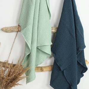 May include: Two waffle weave towels hanging on a wooden rack. The towel on the left is light green and the towel on the right is dark blue.