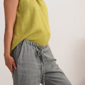 May include: A sleeveless, chartreuse linen top and grey linen trousers. The trousers have a drawstring waist and pockets. The outfit is casual and comfortable, suitable for warm weather.