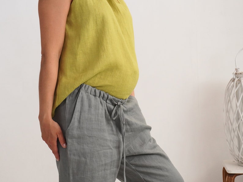 May include: A sleeveless, chartreuse linen top and grey linen trousers. The trousers have a drawstring waist and pockets. The outfit is casual and comfortable, suitable for warm weather.