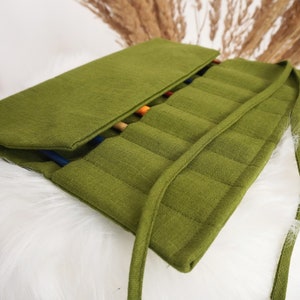 Peut inclure: Un organisateur en tissu vert olive à enrouler, doté de multiples fentes verticales cousues pour le rangement. L'organisateur comprend un long lien en tissu pour sécuriser le rouleau et laisse entrevoir des manches d'outils colorés.