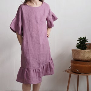 May include: A mauve linen dress with a ruffled hem and short sleeves. The sleeves have a ruffle detail at the edge.