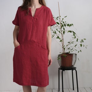 Peut inclure: Une robe en lin rouge avec un col en V et des manches courtes. La robe a deux poches sur le devant.