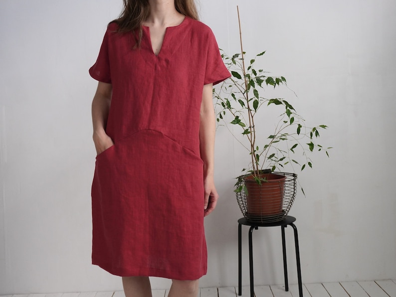 Peut inclure: Une robe en lin rouge avec un col en V et des manches courtes. La robe a deux poches sur le devant.