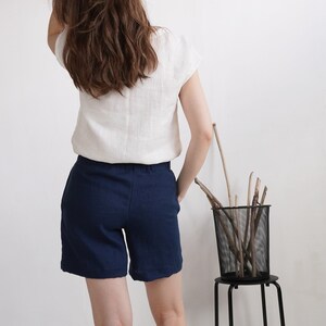 May include: A white short-sleeved top with a round neckline paired with solid navy blue shorts. The top is made of a textured fabric and the shorts feature a simple, clean-cut design with a waistband that sits at the natural waistline.