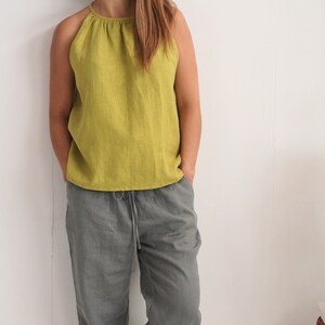 May include: A person wearing a lime green halter top and grey drawstring trousers. The top has a gathered neckline. The trousers are a solid colour. The outfit is made of a lightweight fabric, suitable for warm weather.