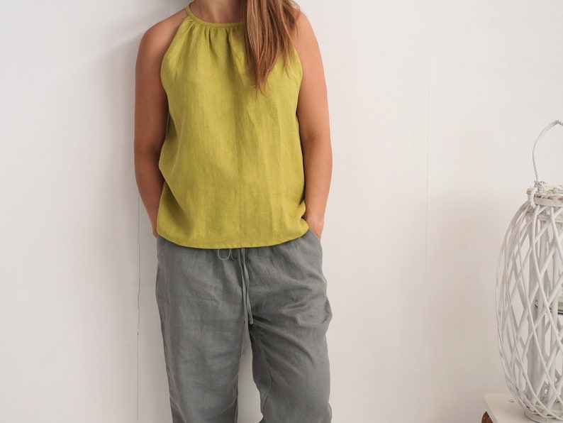 May include: A person wearing a lime green halter top and grey drawstring trousers. The top has a gathered neckline. The trousers are a solid colour. The outfit is made of a lightweight fabric, suitable for warm weather.