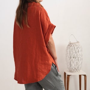 Puede incluir: Una camisa de manga corta color &oacute;xido con cuello y un corte holgado y relajado. La camisa presenta un dobladillo asim&eacute;trico con aberturas laterales y mangas con vuelta. Se combina con un pantal&oacute;n gris, creando un conjunto sencillo.