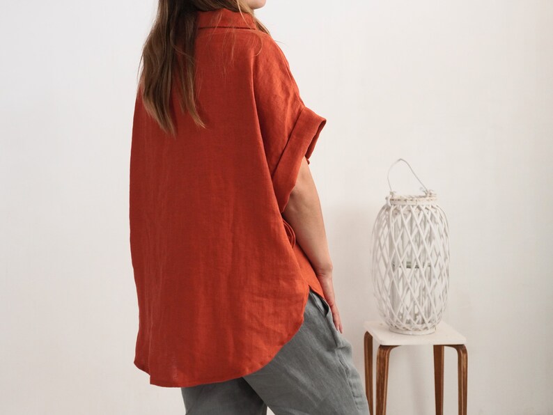 Puede incluir: Una camisa de manga corta color &oacute;xido con cuello y un corte holgado y relajado. La camisa presenta un dobladillo asim&eacute;trico con aberturas laterales y mangas con vuelta. Se combina con un pantal&oacute;n gris, creando un conjunto sencillo.