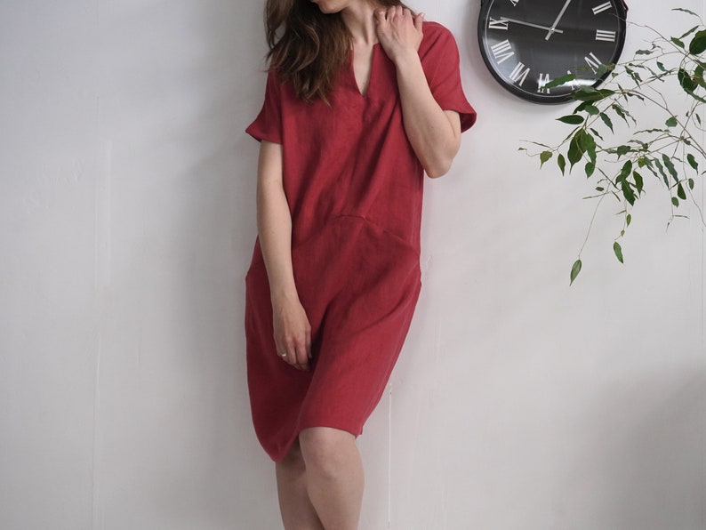 Peut inclure: Une femme portant une robe en lin rouge avec un col en V et des manches courtes. La robe est ample et a une taille l&eacute;g&egrave;rement fronc&eacute;e.