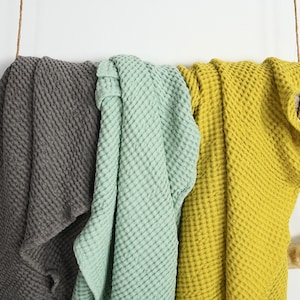 May include: Three waffle weave cotton throws hanging on a wooden branch. The throws are in gray, green, and yellow.