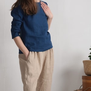 May include: A long-sleeved dark blue top with a round neckline paired with loose-fitting beige trousers featuring side pockets. The top has a straight hemline and the trousers have a relaxed fit, creating a simple two-piece outfit ensemble.