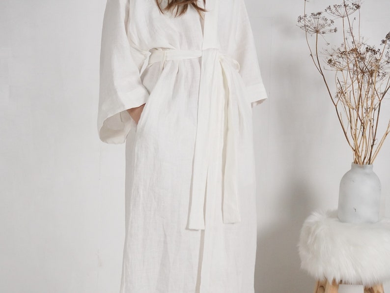 May include: A white linen robe with a long, flowing silhouette and a tie belt. The robe has a relaxed, comfortable fit and is perfect for lounging around the house.