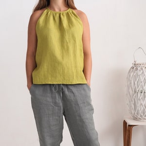 May include: A lime green halter top and grey linen trousers. The top features a gathered neckline and a sleeveless design. The trousers have a drawstring waist. The outfit is casual and comfortable, suitable for warm weather.