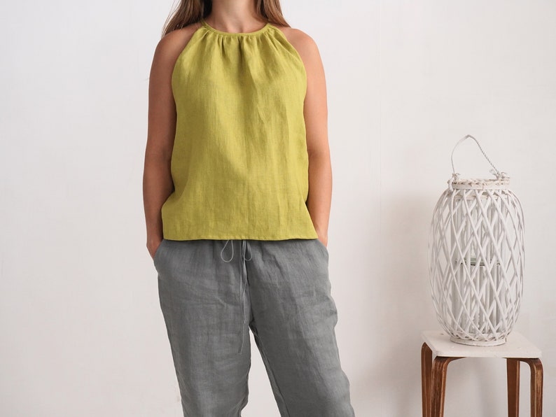 May include: A lime green halter top and grey linen trousers. The top features a gathered neckline and a sleeveless design. The trousers have a drawstring waist. The outfit is casual and comfortable, suitable for warm weather.