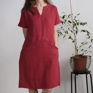 Peut inclure: Une robe en lin rouge avec un col en V et des manches courtes. La robe a deux poches sur le devant et une coupe ample.