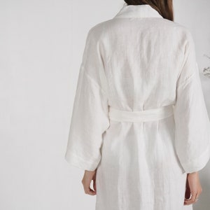 May include: White linen robe with a long sleeve and a sash tie at the waist.