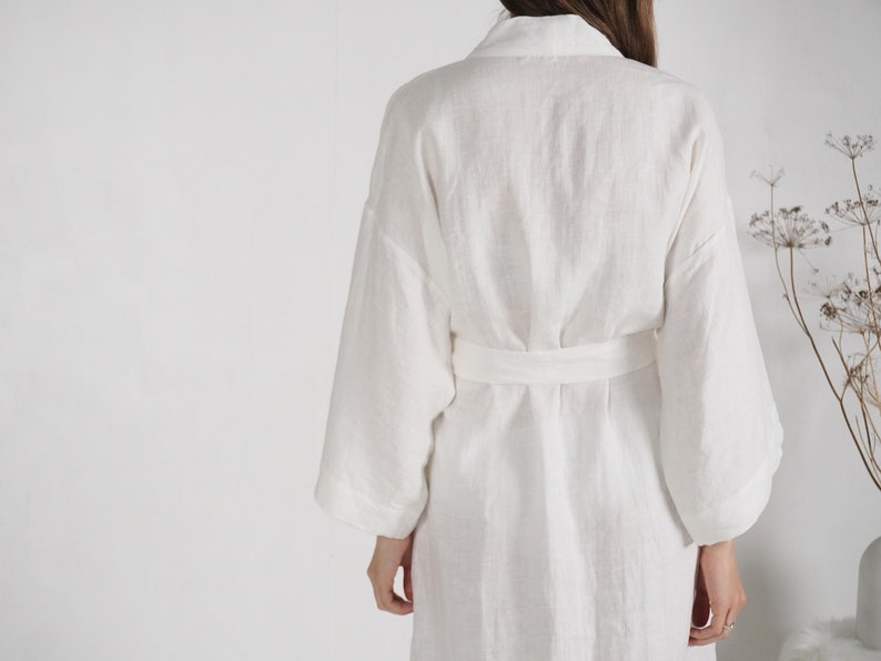 May include: White linen robe with a long sleeve and a sash tie at the waist.