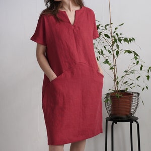 Peut inclure: Une robe en lin rouge avec un col en V et des manches courtes. La robe a deux grandes poches sur le devant.