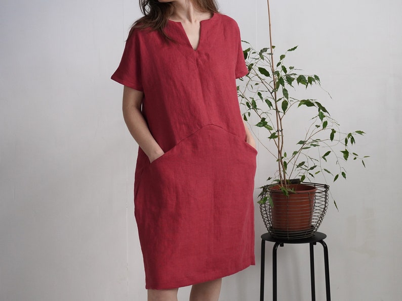 Peut inclure: Une robe en lin rouge avec un col en V et des manches courtes. La robe a deux grandes poches sur le devant.