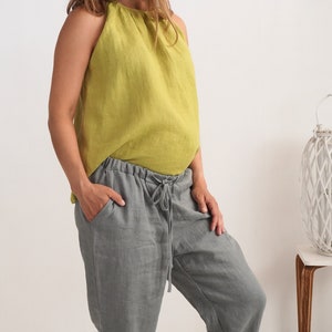 May include: A person wearing a lime green halter top and grey linen trousers with a drawstring waist. The top is sleeveless and the trousers have pockets. The outfit is casual and comfortable.