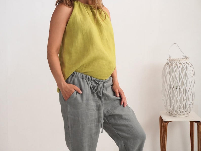 May include: A person wearing a lime green halter top and grey linen trousers with a drawstring waist. The top is sleeveless and the trousers have pockets. The outfit is casual and comfortable.