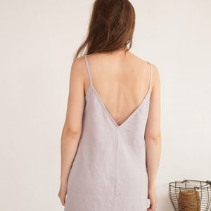Puede incluir: Un vestido lencero de color lavanda claro con tirantes finos y un escote en V profundo en la espalda. La prenda es sin mangas y cae en una silueta recta y sencilla, mostrando una tela de color s&oacute;lido con una textura tejida visible.