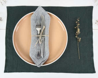 May include: A green linen placemat with a beige round plate and a white and blue striped napkin with a fork and knife on top.