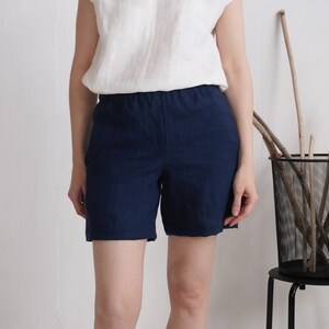 May include: A pair of dark navy blue shorts with an elasticized waistband, paired with a simple white sleeveless top. The shorts feature a clean, straight-leg cut that reaches mid-thigh, crafted from a textured fabric with visible weave details.