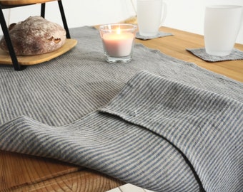 May include: A blue and white striped linen table runner with a candle in a glass jar on a wooden table.