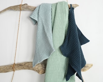 Può includere: Tre asciugamani da cucina a nido d'ape appesi a un ramo di legno rustico. Gli asciugamani sono in tonalità di blu e verde.