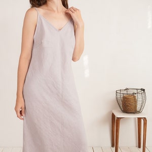 Puede incluir: Un vestido midi sin mangas de color gris lavanda claro con escote en V y tirantes finos. La prenda est&aacute; confeccionada en un tejido texturizado con un corte recto y relajado que llega hasta la altura de la pantorrilla.