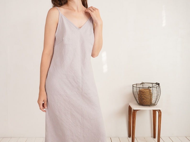 Puede incluir: Un vestido midi sin mangas de color gris lavanda claro con escote en V y tirantes finos. La prenda est&aacute; confeccionada en un tejido texturizado con un corte recto y relajado que llega hasta la altura de la pantorrilla.