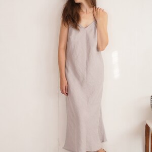 Puede incluir: Un vestido largo sin mangas de color gris claro con escote en V y tirantes finos. La prenda tiene una silueta recta y relajada que llega hasta los tobillos, confeccionada con un tejido texturizado con un patr&oacute;n de tejido visible.