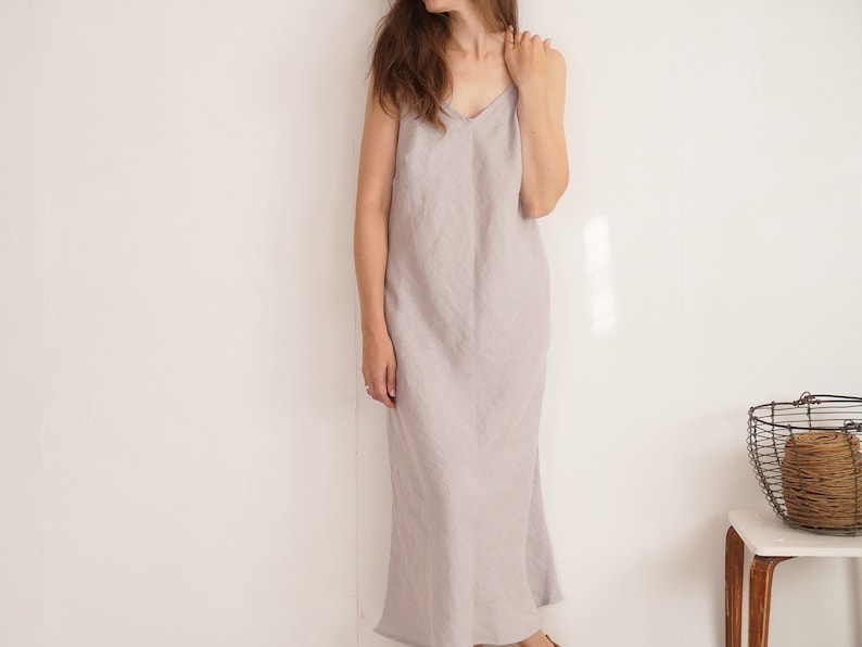 Puede incluir: Un vestido largo sin mangas de color gris claro con escote en V y tirantes finos. La prenda tiene una silueta recta y relajada que llega hasta los tobillos, confeccionada con un tejido texturizado con un patr&oacute;n de tejido visible.
