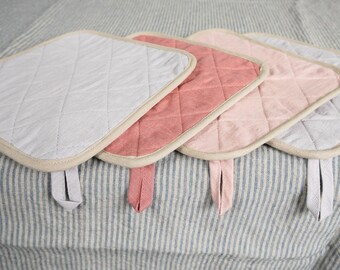 May include: Four quilted pot holders in different colors: gray, pink, light pink, and white. The pot holders have a cream-colored border and a loop handle.