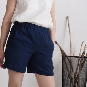 May include: A pair of dark navy blue shorts featuring an elasticized waistband and side pockets. The shorts are constructed from a textured fabric and are paired with a plain white sleeveless top, creating a simple and functional garment combination.