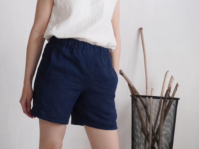 May include: A pair of dark navy blue shorts featuring an elasticized waistband and side pockets. The shorts are constructed from a textured fabric and are paired with a plain white sleeveless top, creating a simple and functional garment combination.