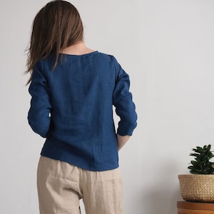 May include: A long-sleeved, deep blue top with a simple round neckline, paired with light beige trousers. The top features a straight hemline and a solid color finish, while the trousers have a relaxed fit and a neutral, light tan appearance.